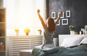 Woman in bedroom sitting on bed and stretching arms up looking relaxed | Healing from trauma | Wellview Counseling | 30076