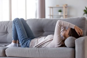 sad teen girl lays on the couch distressed by social distancing during Coronavirus pandemic. She gets online therapy in GA from Wellview Counseling