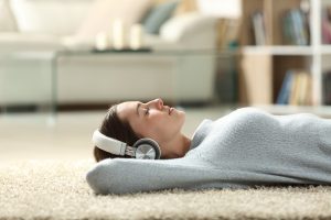teen girl lays on the floor with her large headphones on representing peace and mental wellness. Get help for self-injurious behaviors from working with a therapist who offers teen counseling in Roswell, GA 