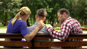 A teen sits with his parents on a park bench. They appear upset as they comfort the teen. This could represent a breakdown in communication teen therapists in Roswell, GA can address. Contact us to learn more about teen counseling in Roswell, GA. Counseling for teens can provide the support your family deserves.