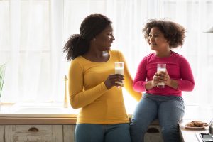 A mother sits with her daughter. Both are enjoying glasses of milk while talking. This could represent a mother connecting with her daughter while talking about a sensitive topic. A child therapist in Roswell, GA can support your family with child counseling, childhood trauma treatment, and more. Contact a child psychologist today!
