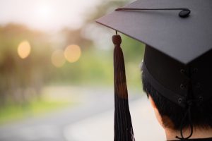 A close up of a graduate standing with their cap and gown as the look into the distance. A young adult therapist in Roswell, GA can provide support with transitioning to what's next. Contact us to learn more about young adult therapy in Roswell, GA today for more info about life transitions therapy and other services. 