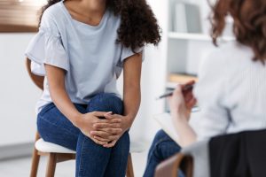 A client sits as they listen to their therapist holding a clipboard. This represents a young adult therapist in Roswell, GA meeting with a client for life transitions therapy, young adult therapy in Roswell, GA, and other services!