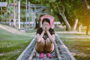A woman crouches on train tracks with her hands over her face. A young adult therapist in Roswell, GA can offer support with life transitions therapy in Roswell, GA and other services.