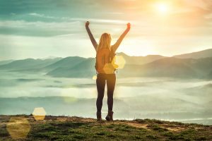 A woman stands proudly on a cliff with her arms toward the sky. A young adult therapist can offer support with young adult therapy in Roswell, GA. Contact a young adult therapist for life transitions therapy in Roswell, GA today!
