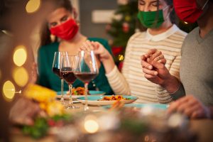 A family wears masks as they join hands for a holiday feast. Young adult therapy in Roswell, GA can offer support during the holiday season. Contact a young adult therapist in Roswell, GA to learn more about life transitions therapy and other services. 30076