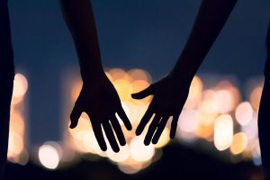 Photo of two hands meeting in the dark representing two people who have developed a closer relationship as they've learned DBT skills and begun to set healthy boundaries.
