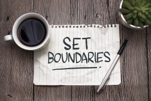 A paper with the words "set boundaries" as well as a pen and cup of coffee representing the importance of learning skills to effectively communicate your boundaries in a relationship.