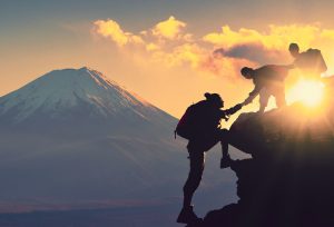 Photo of three young friends helping each other climb a mountain. This photo represents how teen therapists can help teens and young adults navigate conflict with their friends.