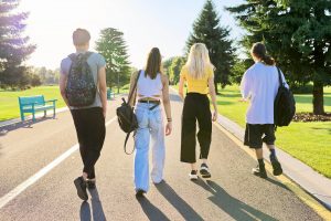 Photo of four friends walking down a paved path in a park. This photo represents how working with a young adult therapist in Roswell, GA help you navigate relationships and assert your needs.