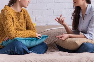 Photo of a girl and her mother sitting on their bed talking. This photo represents how young adult therapy in GA can help you ask for what you need as a young adult.