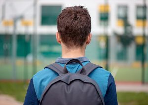 Photo of a boy wearing a backpack looking at a school. This photo represents how anxiety counseling can in roswell, ga can help teens overcome school anxiety.