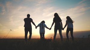 Photo of a family of four holding hands and walking through a field. This photo represents how family therapy in San antonio, tx can help your family overcome the challenges you're facing.
