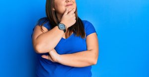 Photo of a woman against a blue backdrop posing as if she's thinking. This represents thinking if Online Counseling in Georgia is right for you.
