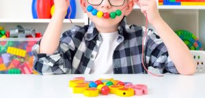 Shows a little boy making a happy face with beads. Represents how play therapy in Roswell, GA can help your child with their emotions