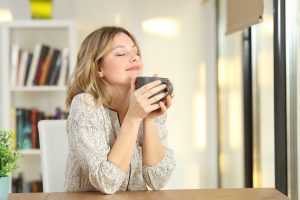 Shows a young woman with her eyes closed enjoying a hot drink after a good night of sleep. Represents how sleep therapy in Roswell, GA can help you feel good in the morning.